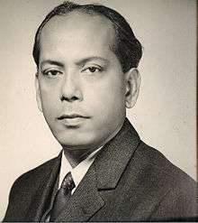 Black-and-white photo of the head and shoulders of a middle-aged man. Brown skin, receding hairline, short dark hair. He is wearing a suit and looking at the camera with a calm but determined expression.
