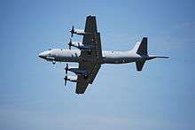 A grey, four engined aircraft viewed from below while it is in flight