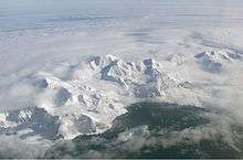 Aerial view of a range of icy mountains with a coastline visible in the foreground