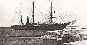 Three-masted ship with funnel to rear, anchored by the bow to an ice shelf