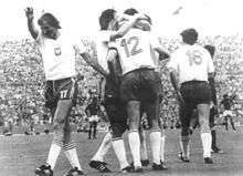 Football players in white shirts and dark shorts celebrate together