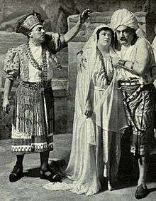 Three figures in exotic costumes; to the right a man and a woman embrace, while on the left another man addresses them, left arm raised perhaps in a gesture of blessing