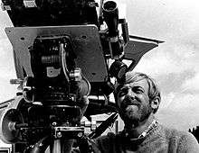 Black and white photograph; a man squints into the telescopic eyepiece of a large mechanical device.