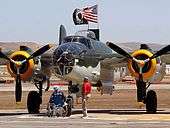 Closeup of bomber on tarmac with two older men, one in a wheelchair looking on