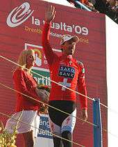 A man walking across a stage while waving and wearing a red jersey