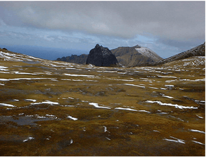 A bare stretch of land with ice and snow patches, leading to rocky hills in the background