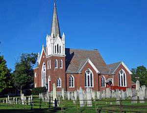 A brick church with white tower and a cemetery in front