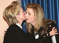 A man in an Ottoman army uniform, sporting a full moustache, and wearing a wool hat and round spectacles. He carries what appear to be gloves in his left hand. His right arm is bent and his right hand rests on the small of his back.