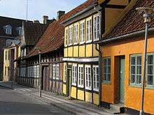 One and two storied attached buildings, with steeply pitch roofs, front directly on the side walk and street. They are made of combinations of plaster, timber and brick, with paned glass windows.