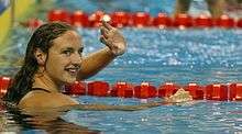 A female swimmer with head above the water, waiving.