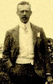Photo of Burnham's brother Mather Howard Burnham. Howard is wearing a suit and tie and standing with his right hand in his pocket.