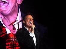 A man is facing right while holding a microphone with his right hand.