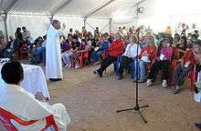 A color photo of a priest offering mass in a white tent with dirt floor for the workers and family members at San Jose Mine