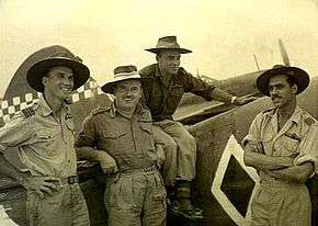 Three-quarter informal portrait of four men in military uniforms with slouch hats in front of a military aircraft
