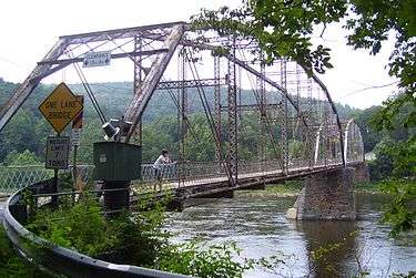 A view along a bridge with metal girders overhead and a wooden deck