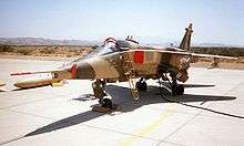 A Jaguar in desert camouflage scheme parked on hardstanding. The cockpit canopy is just open, with covers on the air intakes and on the nose probe, and a ladder giving access to the cockpit