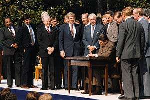 Rangel and about fourteen other men standing around a table, where President Ronald Reagan signs a bill