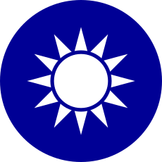 A blue circular emblem on which sits a white sun composed of a circle surrounded by 12 rays.