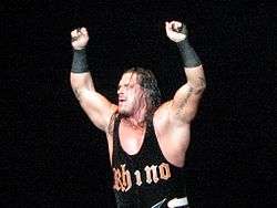 An adult white male wearing black standing in a wrestling ring.