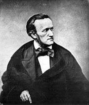 Man wearing a cloak and an outsized bow tie, facing to the right with a severe expression