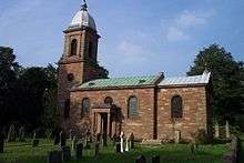 A Georgian church seen from the south. On the left is the tower with a cupola, the nave has a circular window, two round-headed windows and a porch supported by columns, and the chancel has a single round-headed window