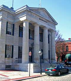 The front of a granite building, which has four columns supporting a triangular pediment.