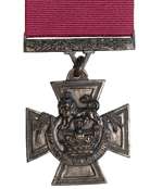 A bronze cross pattée bearing the crown of Saint Edward surmounted by a lion with the inscription FOR VALOUR. A crimson ribbon is attached